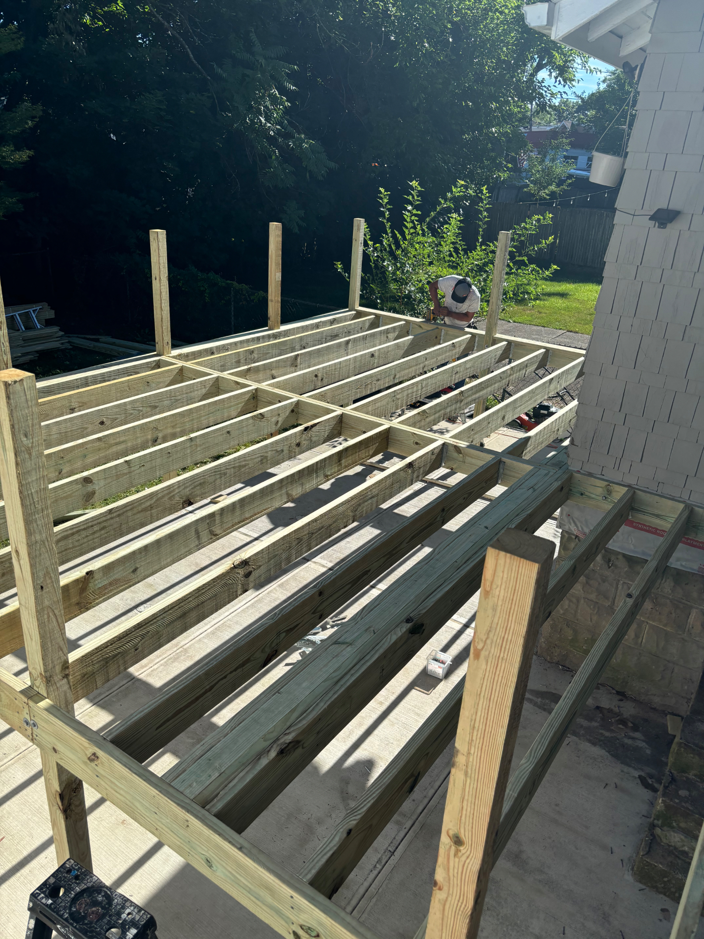 Pressure-treated deck framing in progress with joists, posts, and railing supports installed over concrete pad