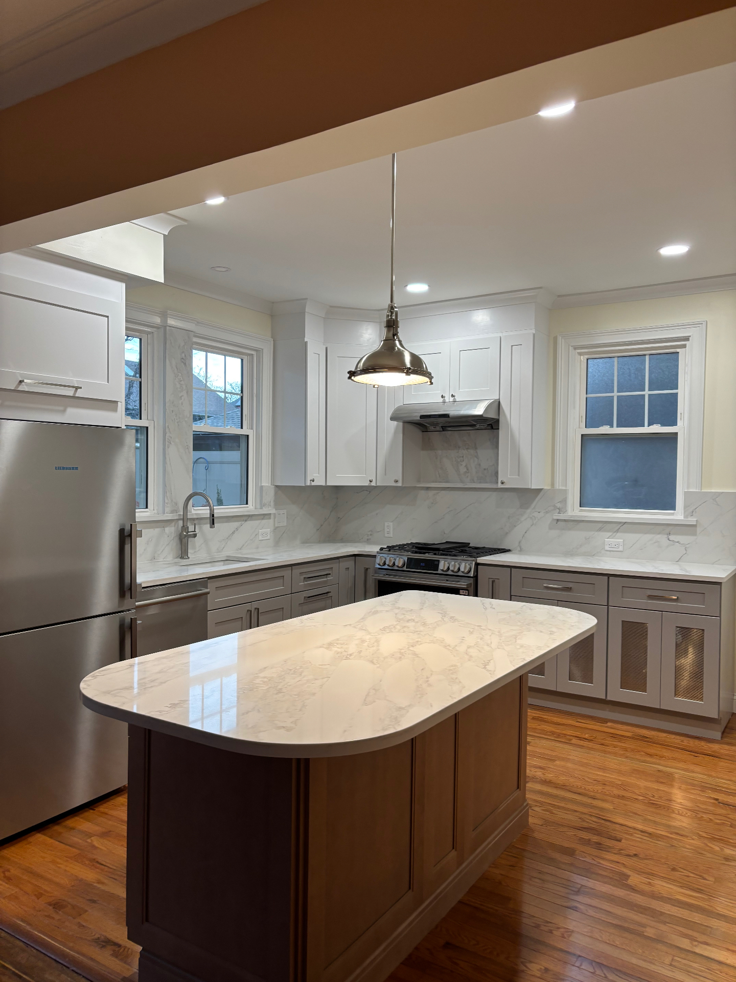 Finished modern kitchen remodel with white shaker cabinets, marble countertops and backsplash, quartz island, stainless appliances, and refinished hardwood floors