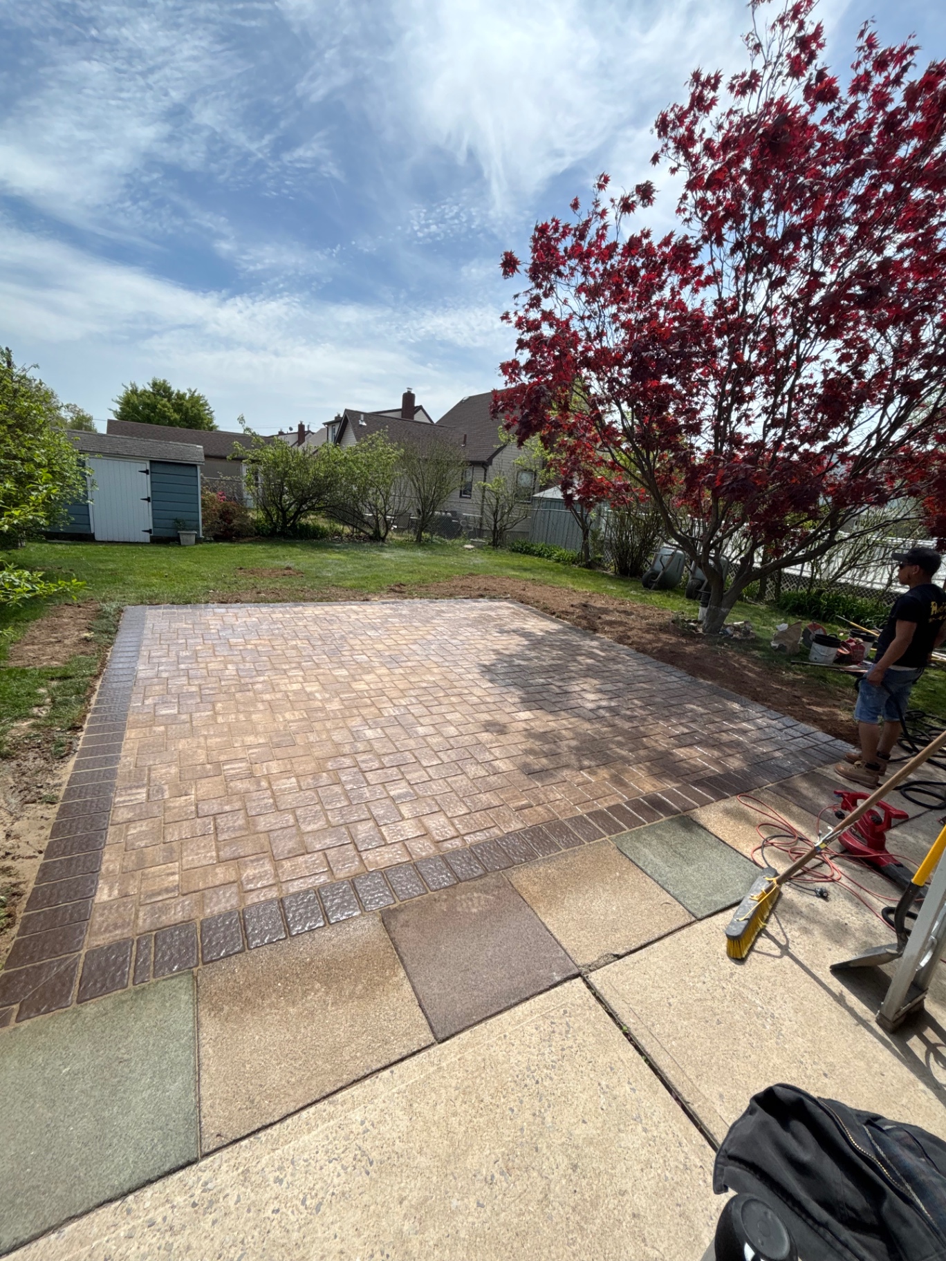 Finished backyard paver patio with darker border course under a Japanese maple tree