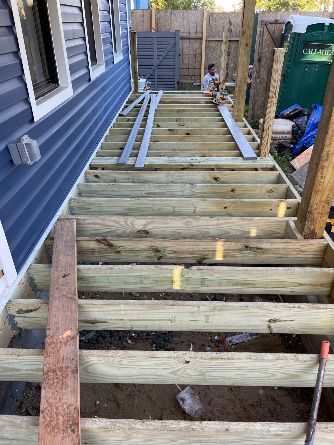 Pressure-treated porch framing and joists being built alongside blue-sided home