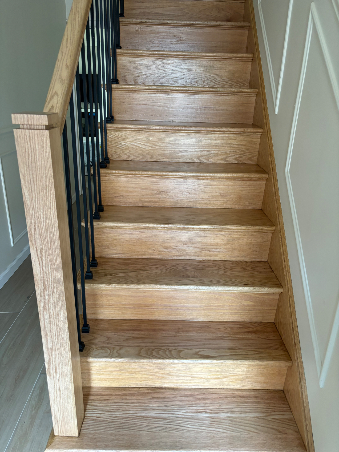 Finished custom red oak staircase with solid oak treads and risers, oak newel post and handrail, and black wrought-iron balusters