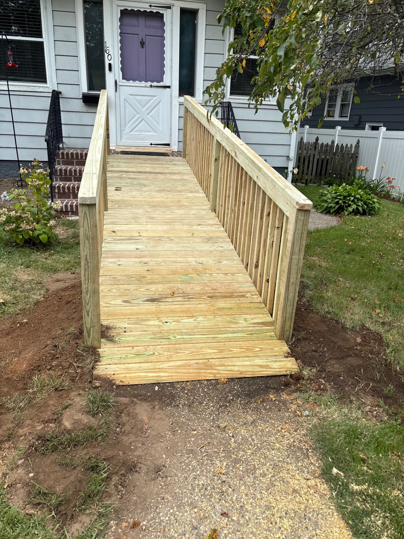Front view of newly built pressure-treated wheelchair ramp leading up to home's front door with full handrails