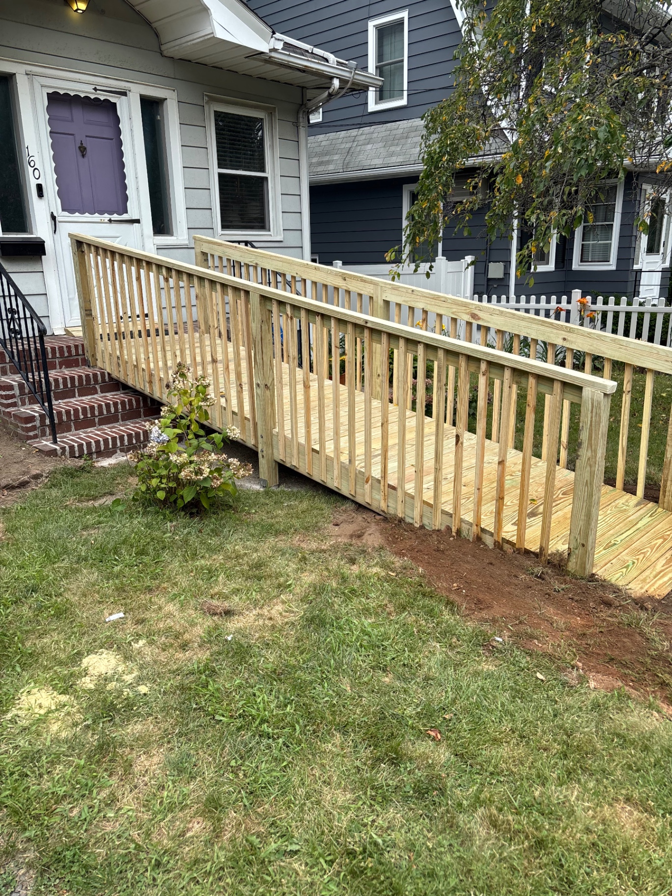 Side view of custom wheelchair accessibility ramp showing gentle slope, vertical balusters, and handrails alongside home